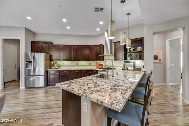 kitchen featuring a breakfast bar, a sink, open shelves, stainless steel fridge, and wall chimney range hood