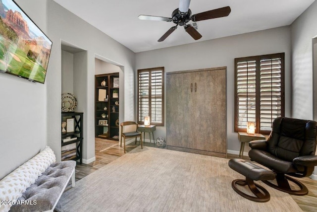 sitting room with baseboards, wood finished floors, and a ceiling fan