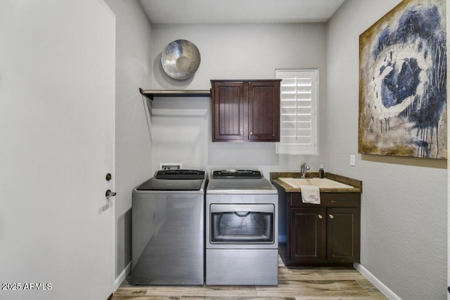 laundry room featuring baseboards, washing machine and clothes dryer, light wood-style flooring, cabinet space, and a sink