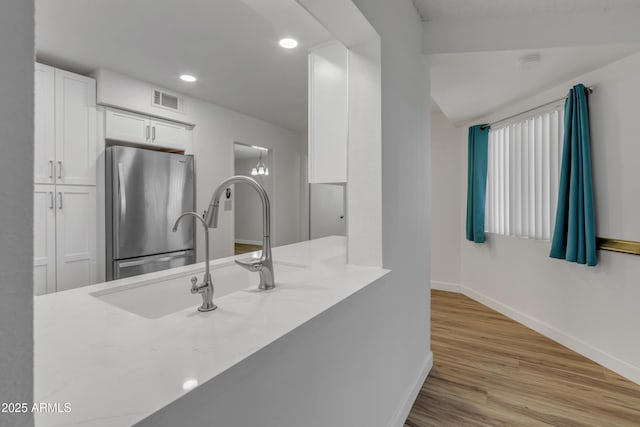 kitchen with a sink, freestanding refrigerator, white cabinetry, wood finished floors, and visible vents
