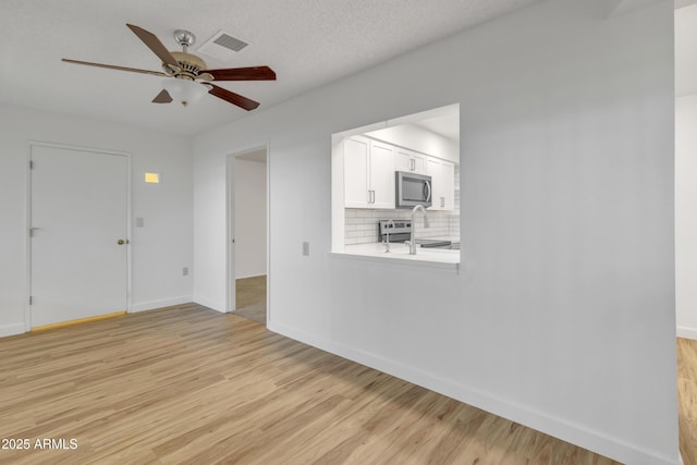 unfurnished living room with a textured ceiling, light wood-style flooring, visible vents, baseboards, and ceiling fan