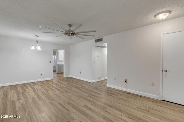 empty room featuring a textured ceiling, light wood-style flooring, visible vents, baseboards, and a ceiling fan