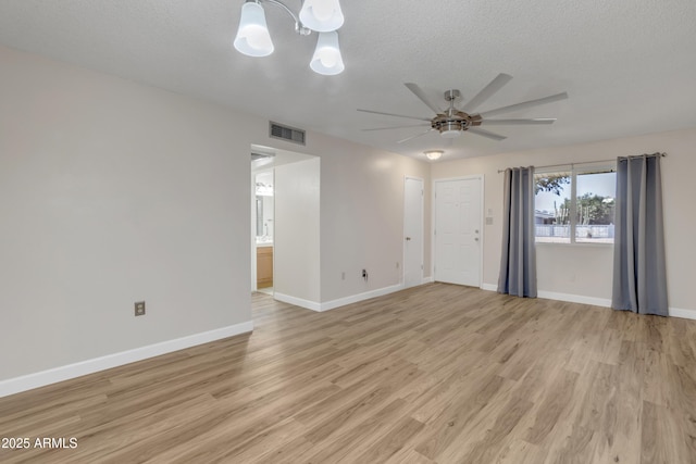 empty room with a textured ceiling, visible vents, light wood finished floors, baseboards, and ceiling fan with notable chandelier