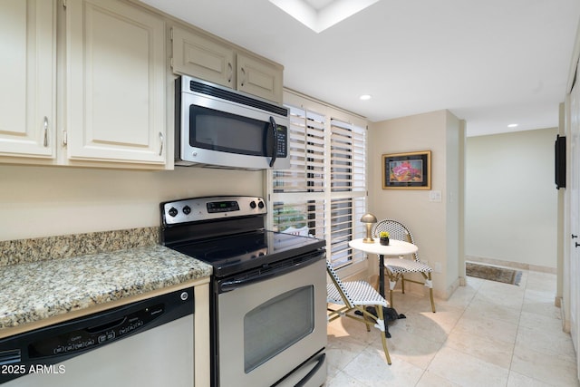 kitchen with cream cabinets, light tile patterned floors, light stone countertops, and stainless steel appliances