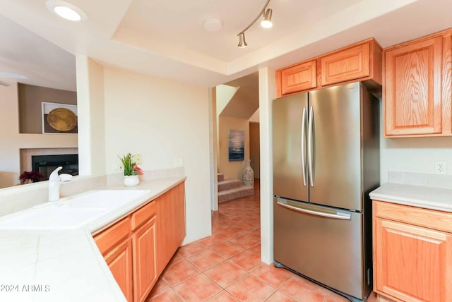 kitchen with sink, light brown cabinets, a raised ceiling, light tile patterned flooring, and stainless steel refrigerator