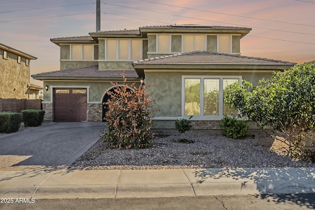 prairie-style house featuring brick siding, fence, stucco siding, decorative driveway, and a garage