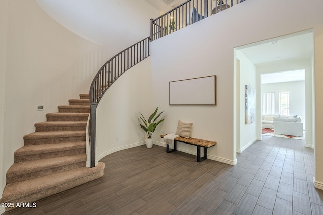 staircase featuring baseboards, a high ceiling, and wood tiled floor