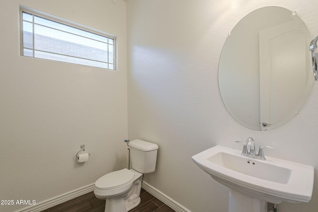 half bathroom featuring a sink, toilet, baseboards, and wood tiled floor