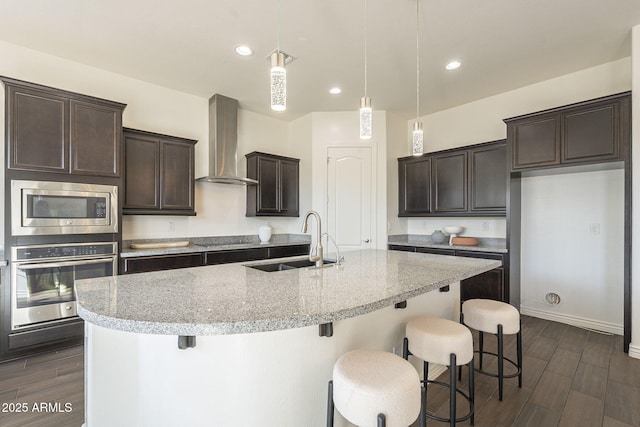 kitchen with wood finish floors, appliances with stainless steel finishes, wall chimney range hood, and a sink