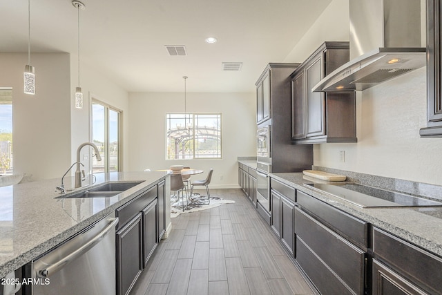 kitchen featuring visible vents, a sink, appliances with stainless steel finishes, wall chimney exhaust hood, and light stone countertops