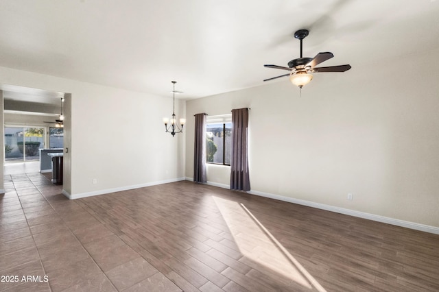 empty room with dark hardwood / wood-style floors, ceiling fan with notable chandelier, and plenty of natural light