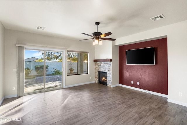 unfurnished living room featuring ceiling fan, hardwood / wood-style flooring, and a stone fireplace