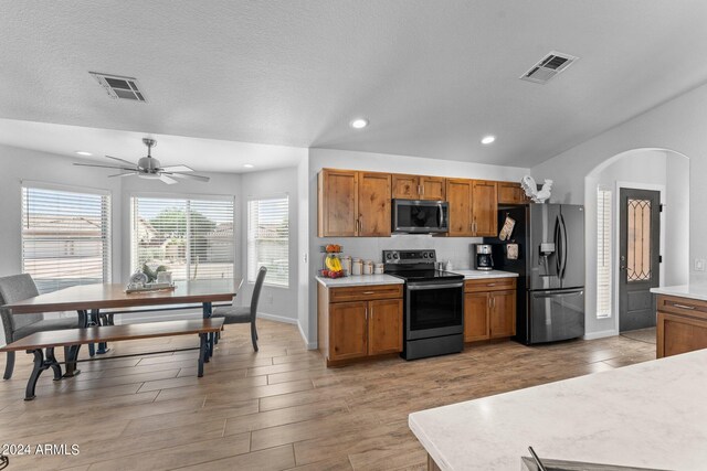 kitchen with appliances with stainless steel finishes, a textured ceiling, ceiling fan, and light hardwood / wood-style floors