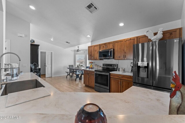 kitchen with appliances with stainless steel finishes, light hardwood / wood-style floors, sink, lofted ceiling, and ceiling fan