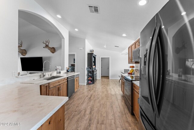 kitchen with vaulted ceiling, light hardwood / wood-style flooring, appliances with stainless steel finishes, kitchen peninsula, and sink