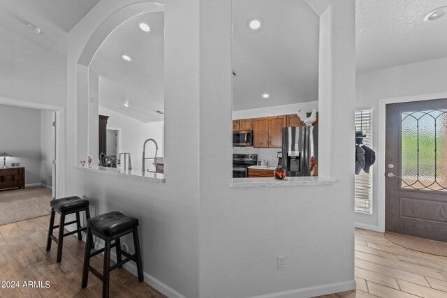 kitchen featuring kitchen peninsula, a breakfast bar, appliances with stainless steel finishes, lofted ceiling, and light hardwood / wood-style floors