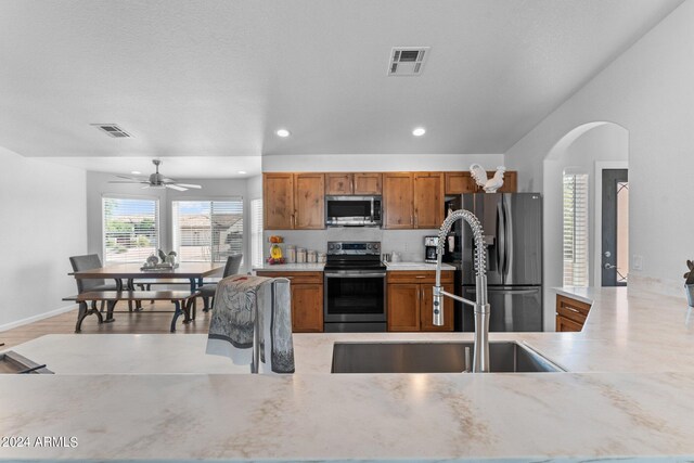 kitchen with light wood-type flooring, tasteful backsplash, sink, ceiling fan, and appliances with stainless steel finishes