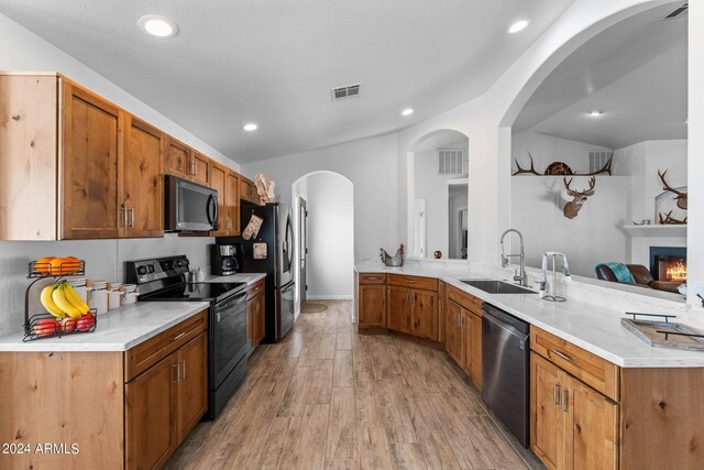 kitchen with black appliances, light hardwood / wood-style flooring, kitchen peninsula, sink, and lofted ceiling