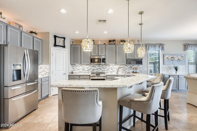 kitchen featuring a center island with sink, appliances with stainless steel finishes, gray cabinets, hanging light fixtures, and a breakfast bar