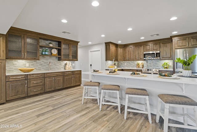 kitchen featuring decorative backsplash, stainless steel appliances, light wood-type flooring, a kitchen bar, and sink