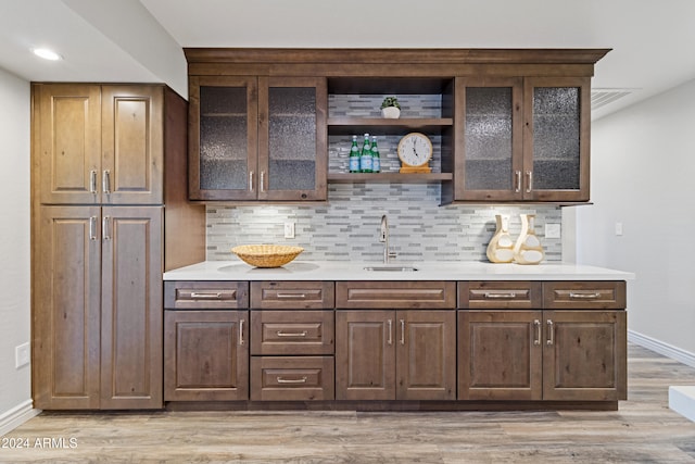 bar with light wood-type flooring, backsplash, dark brown cabinetry, and sink