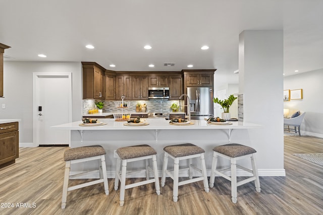 kitchen featuring appliances with stainless steel finishes, light wood-type flooring, a breakfast bar area, and tasteful backsplash