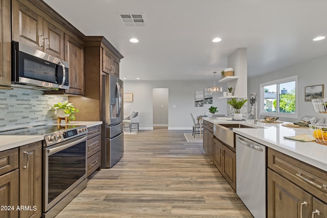 kitchen featuring light wood-type flooring, tasteful backsplash, sink, appliances with stainless steel finishes, and decorative light fixtures