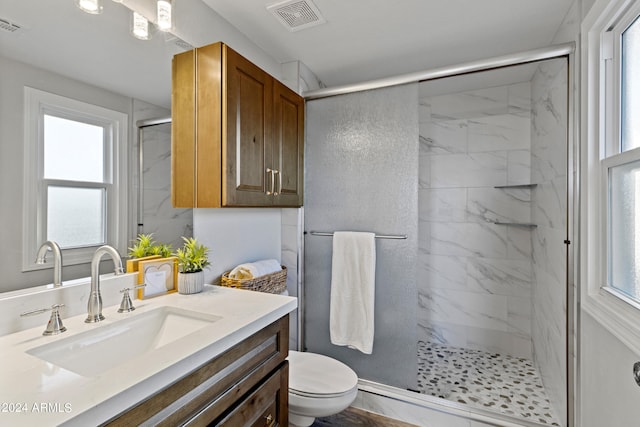 bathroom featuring a wealth of natural light, a shower with door, vanity, and toilet