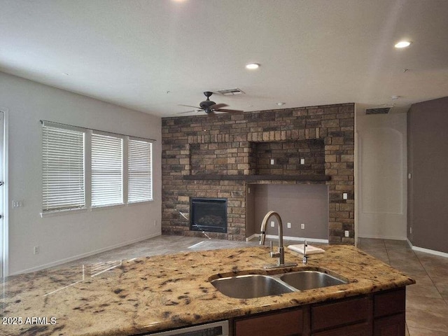 kitchen featuring a sink, visible vents, baseboards, light stone countertops, and a ceiling fan