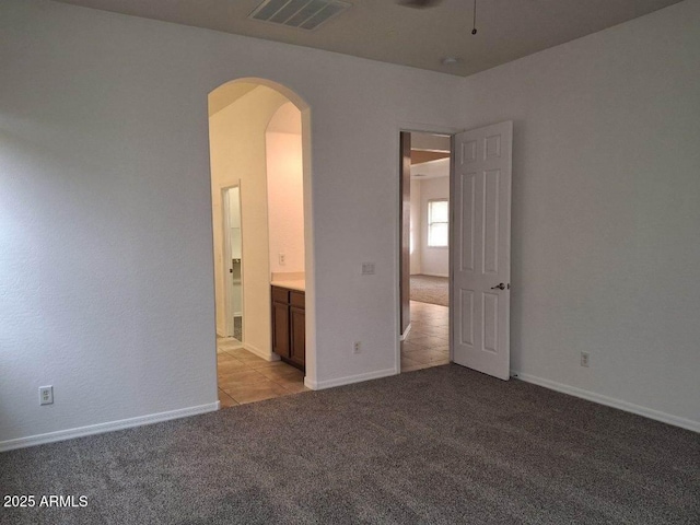 unfurnished bedroom with visible vents, ensuite bathroom, baseboards, arched walkways, and light carpet