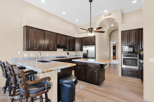 1940 N Stevens Cir, Mesa, AZ 85205 - kitchen with black appliances, ventilation hood, arched walkways, a breakfast bar, and dark brown cabinetry