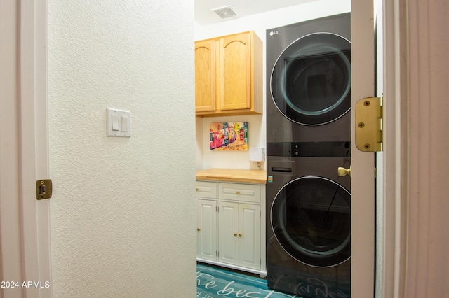 clothes washing area with stacked washer / drying machine and cabinets