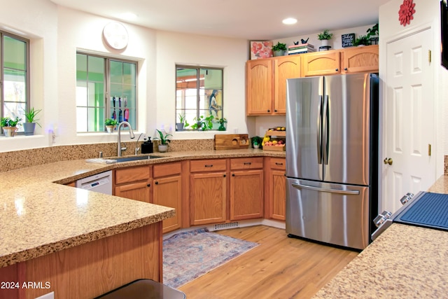 kitchen with dishwasher, sink, light stone countertops, light hardwood / wood-style floors, and stainless steel refrigerator