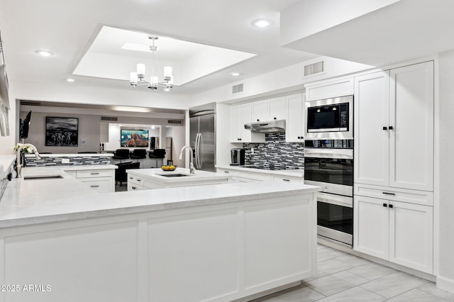 kitchen with pendant lighting, built in appliances, kitchen peninsula, and sink