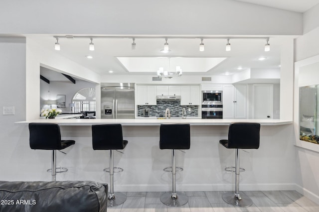 kitchen featuring white cabinetry, built in appliances, tasteful backsplash, a kitchen bar, and kitchen peninsula