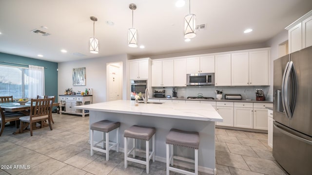 kitchen with white cabinets, appliances with stainless steel finishes, pendant lighting, and an island with sink