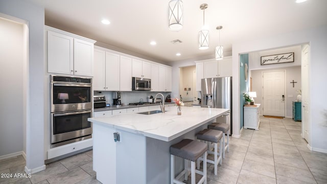 kitchen featuring a kitchen island with sink, sink, decorative light fixtures, white cabinetry, and stainless steel appliances