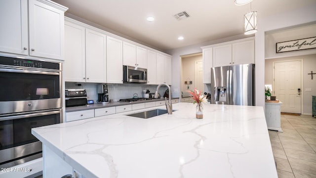 kitchen with light stone countertops, appliances with stainless steel finishes, white cabinetry, and hanging light fixtures