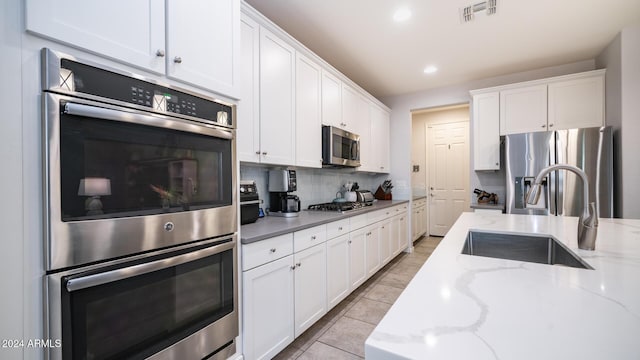 kitchen with white cabinets, sink, decorative backsplash, appliances with stainless steel finishes, and light stone counters