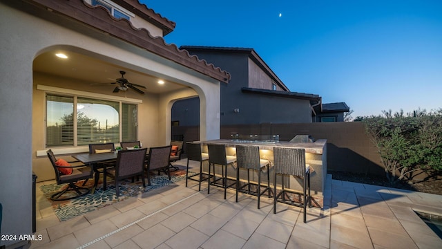 patio terrace at dusk featuring ceiling fan and an outdoor bar