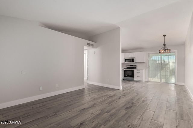 unfurnished living room with lofted ceiling, visible vents, baseboards, and wood finished floors