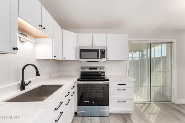 kitchen featuring light wood finished floors, stainless steel appliances, white cabinetry, a sink, and light stone countertops