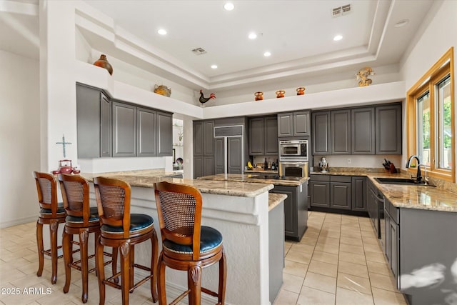 kitchen featuring sink, kitchen peninsula, a towering ceiling, stainless steel appliances, and light stone countertops