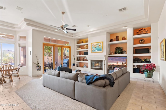 tiled living room with a raised ceiling, ceiling fan, and built in shelves