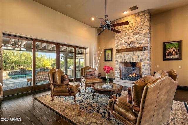 living area featuring visible vents, a fireplace, a high ceiling, wood finished floors, and a ceiling fan