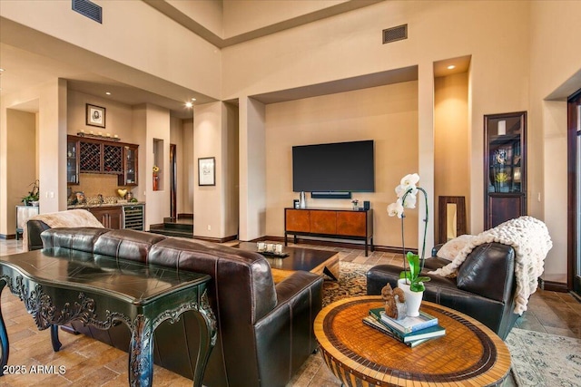 living area featuring beverage cooler, visible vents, bar area, and a towering ceiling