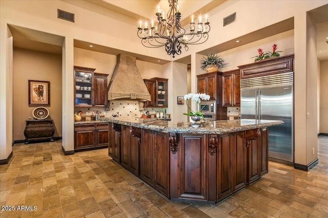 kitchen with visible vents, built in appliances, custom exhaust hood, and tasteful backsplash