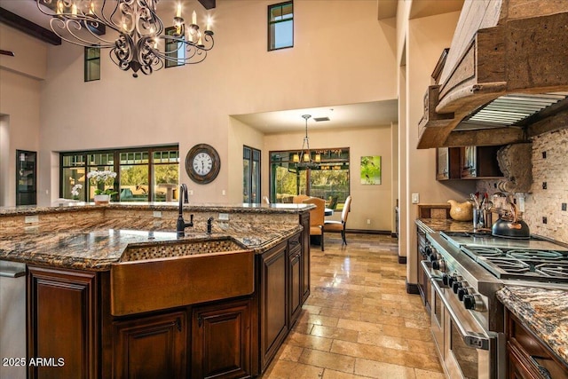 kitchen with under cabinet range hood, range with two ovens, stone tile flooring, a notable chandelier, and a sink