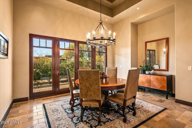 dining area with stone tile flooring, a high ceiling, baseboards, and a chandelier