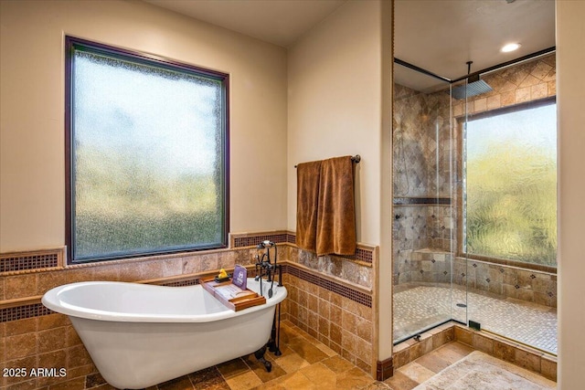 full bath featuring tile walls, a soaking tub, a tile shower, and wainscoting